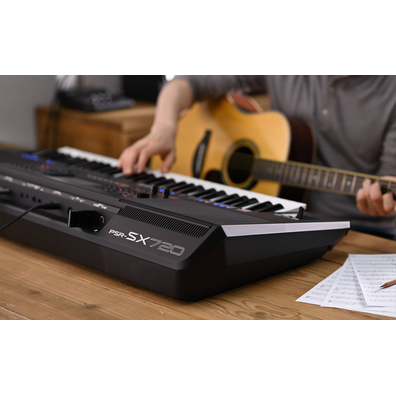 Photo of a person playing Yamaha Arranger Workstation PSR-SX720 while holding a guitar